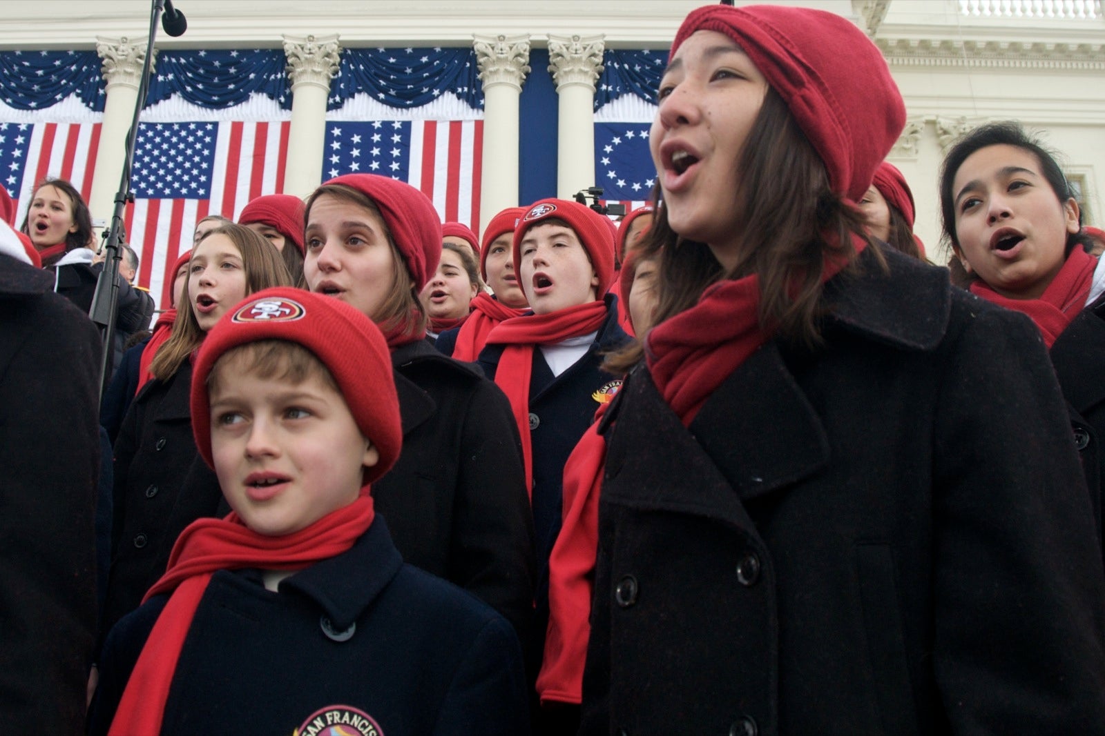 San Francisco chorus girls and boys in red hats and scarves perform.