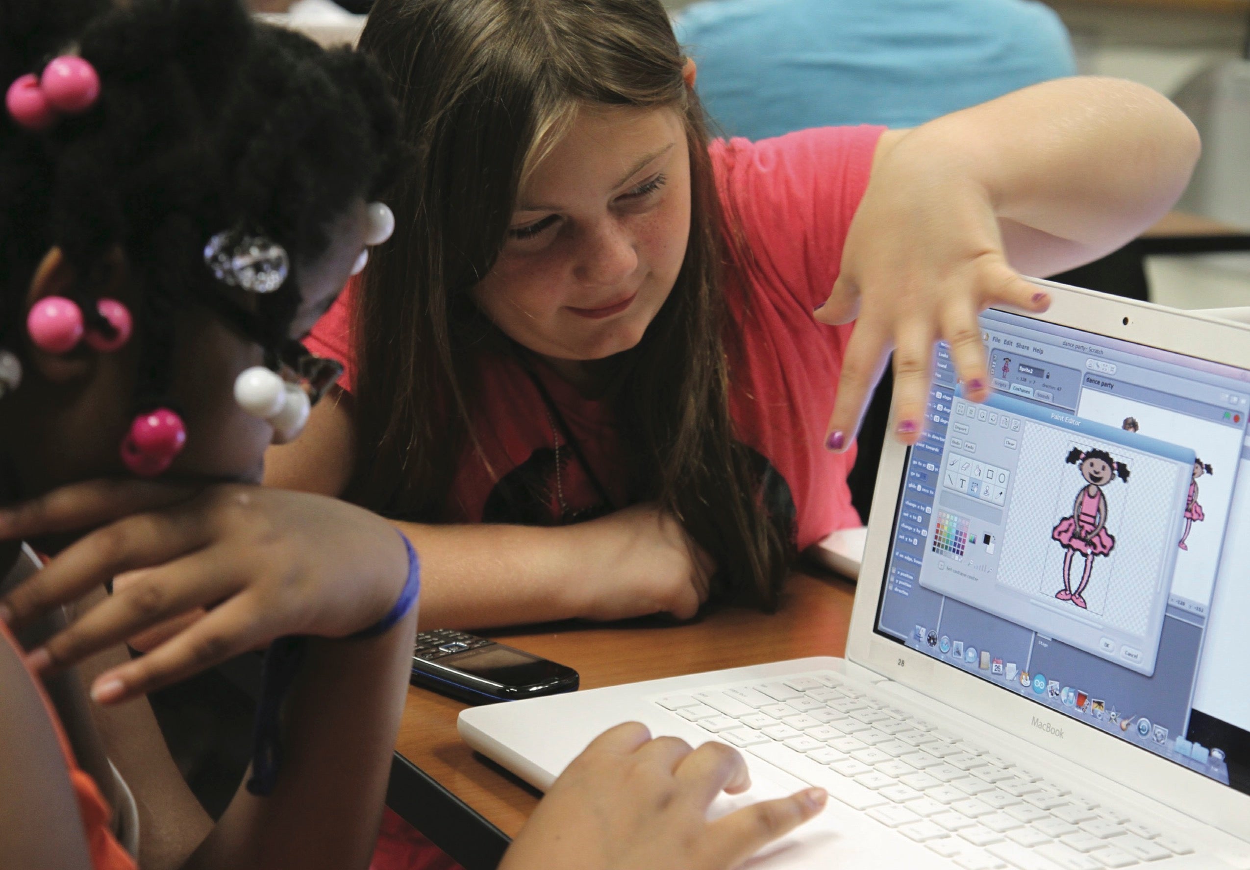 Two girls sit at a laptop designing a digital character.