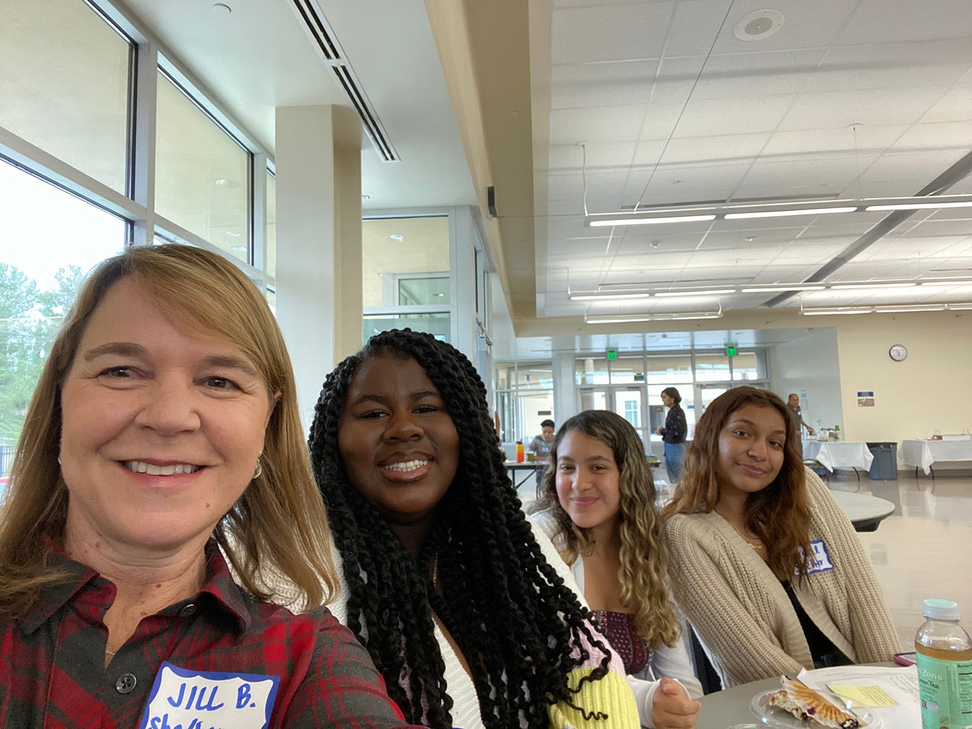 A group of four women education leaders in a school cafeteria smile at the camera.