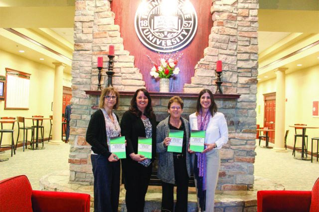 Four women stand in front of a decorative wall with a newly launched book in their hands.